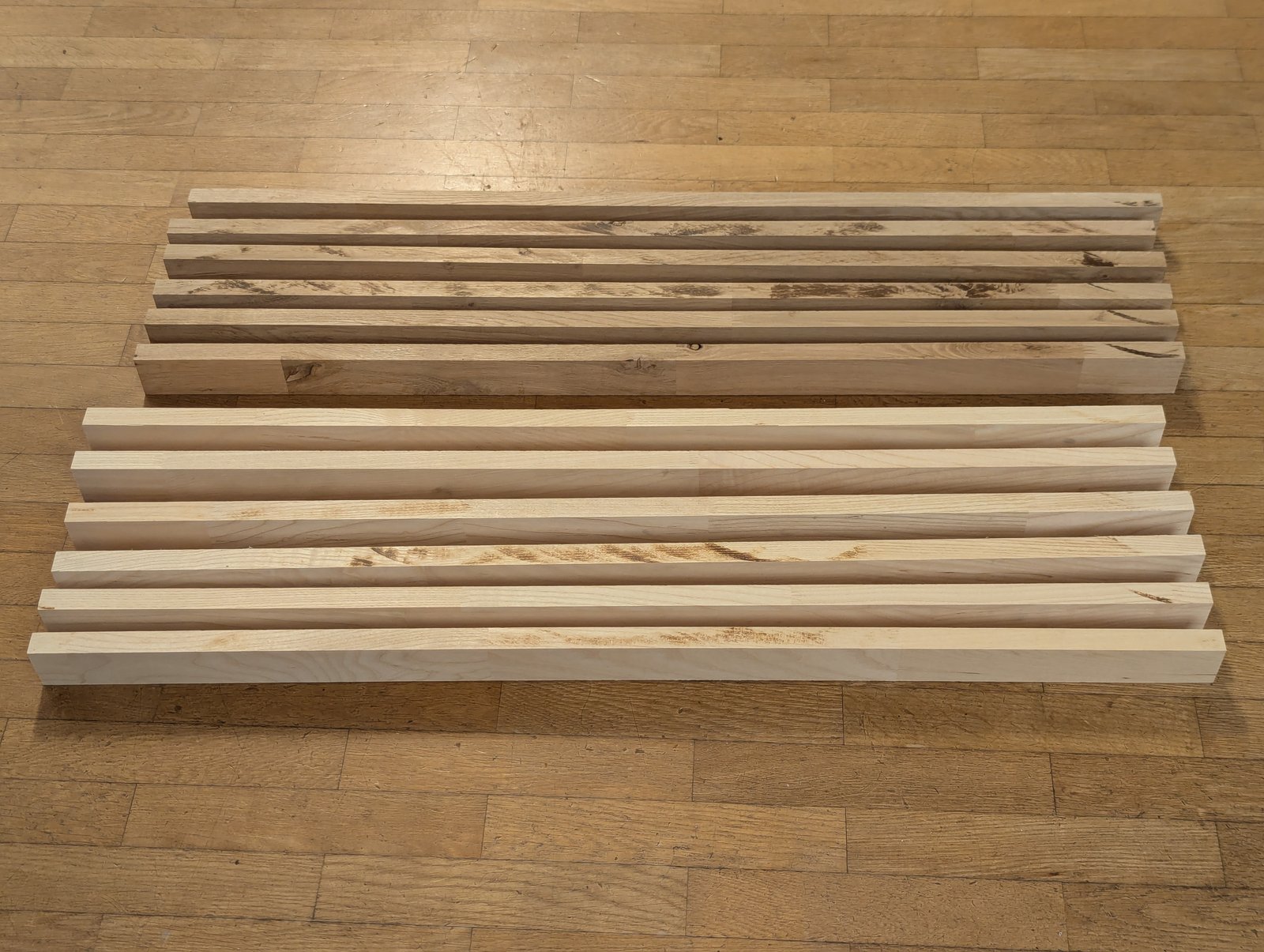 Tasseaux de bois clairs et foncés alignés sur le parquet.