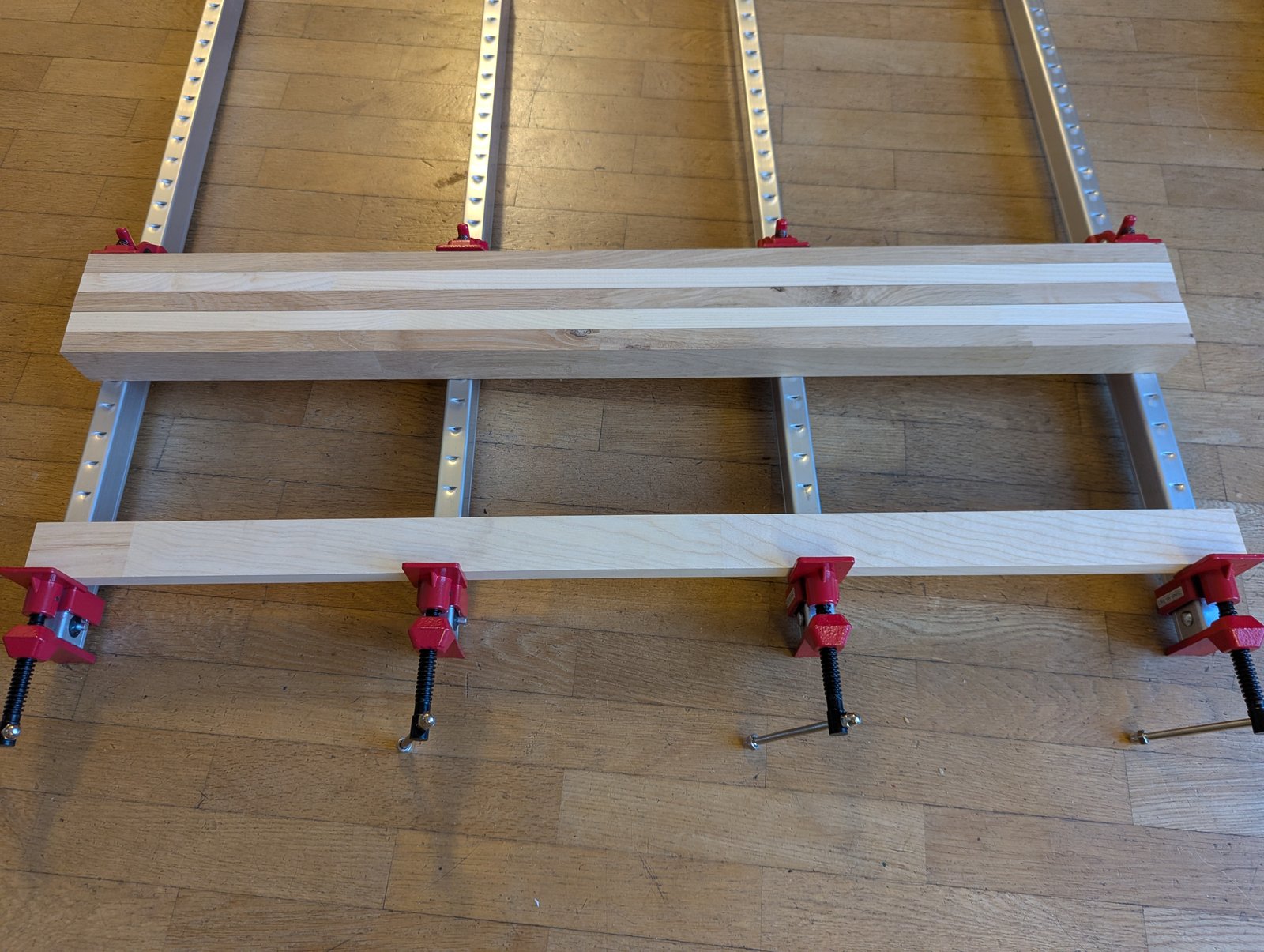 Bandes de bois de deux teintes disposées sur quatre longs serre-joints.