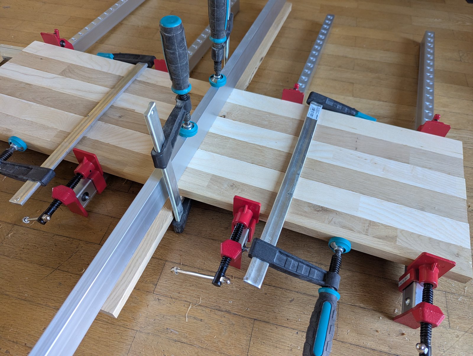 Panneau assemblé sous plusieurs serre-joints, traversé par une règle métallique.