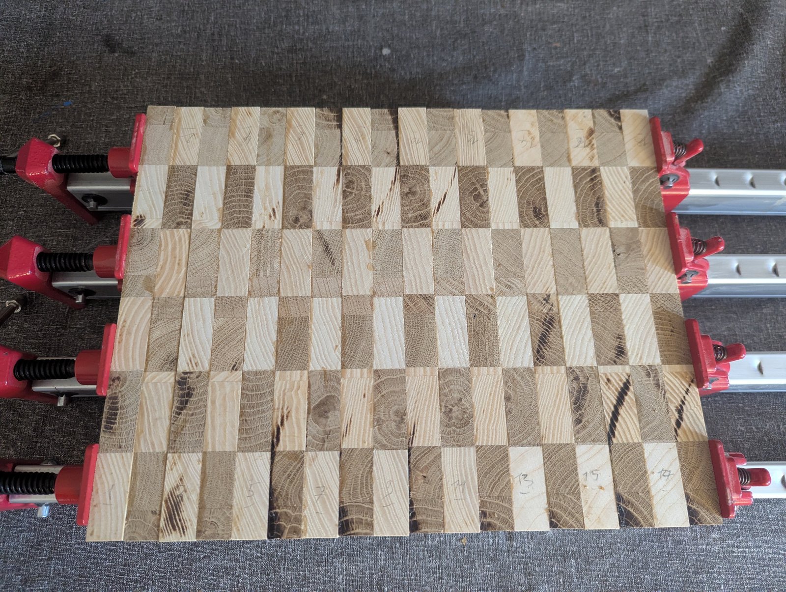 Planche carrée en bois de bout, avec des blocs clairs et foncés alternés, serrée dans quatre presses.